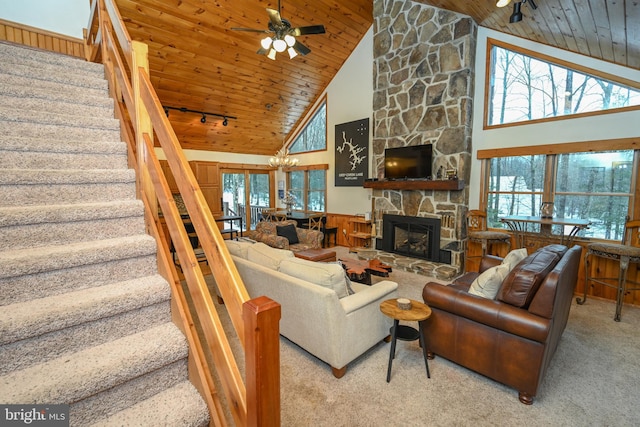 living room with carpet floors, high vaulted ceiling, ceiling fan with notable chandelier, a stone fireplace, and wood ceiling