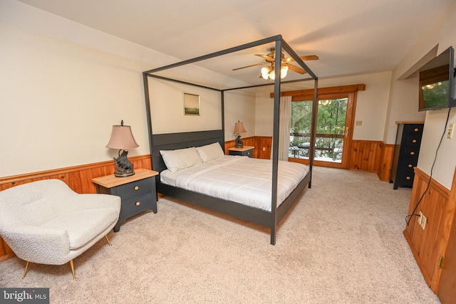 bedroom featuring wooden walls, ceiling fan, light carpet, and access to outside