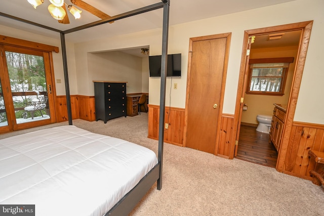 bedroom with light colored carpet, ensuite bath, ceiling fan, and wooden walls