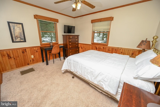 bedroom with ceiling fan, ornamental molding, wooden walls, and multiple windows