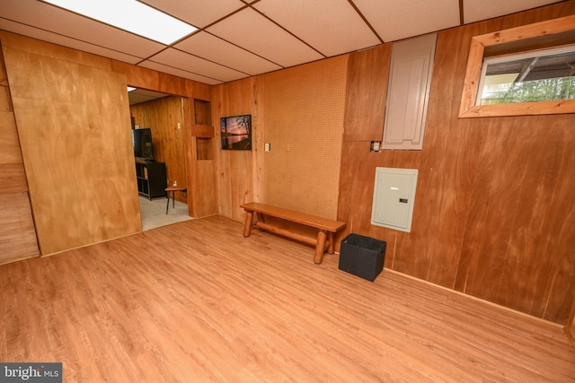 interior space with a paneled ceiling, wood walls, light wood-type flooring, and electric panel