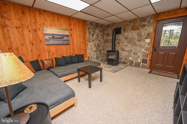 carpeted living room featuring a paneled ceiling, wooden walls, and a wood stove