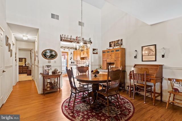 dining space featuring a chandelier, a towering ceiling, and light hardwood / wood-style floors