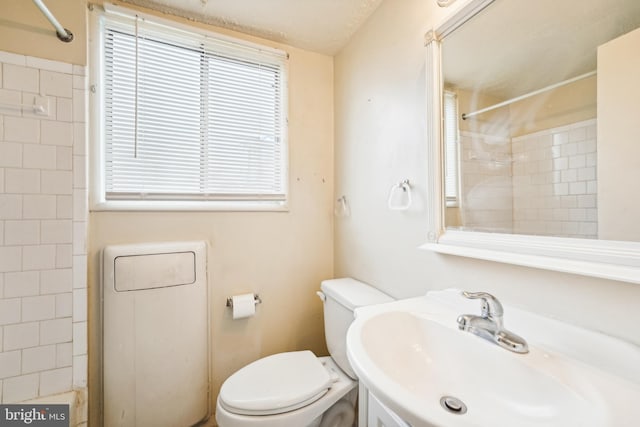 bathroom with a tile shower, a textured ceiling, toilet, and sink