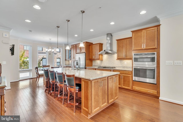 kitchen with a kitchen island with sink, wall chimney exhaust hood, stainless steel appliances, and light wood-type flooring