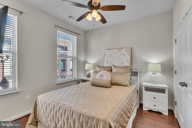 bedroom with ceiling fan, dark wood-type flooring, and multiple windows