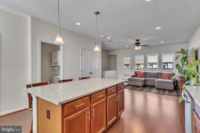 kitchen with decorative light fixtures, a kitchen island, dark wood-type flooring, and a breakfast bar area