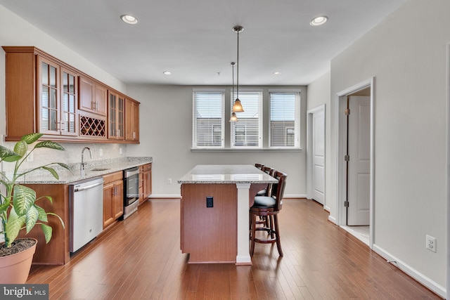 kitchen featuring dishwasher, a center island, hanging light fixtures, light stone counters, and hardwood / wood-style floors