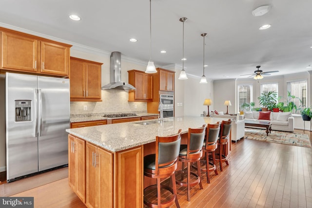 kitchen with a center island with sink, pendant lighting, wall chimney range hood, and appliances with stainless steel finishes