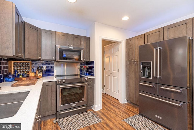 kitchen featuring decorative backsplash, dark brown cabinetry, stainless steel appliances, dark wood-type flooring, and sink