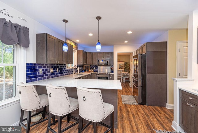 kitchen with kitchen peninsula, stainless steel appliances, a breakfast bar area, and dark wood-type flooring