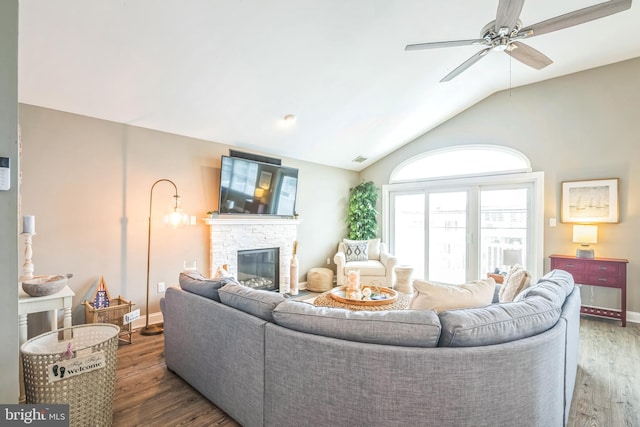 living room featuring ceiling fan, a stone fireplace, lofted ceiling, and dark wood-type flooring