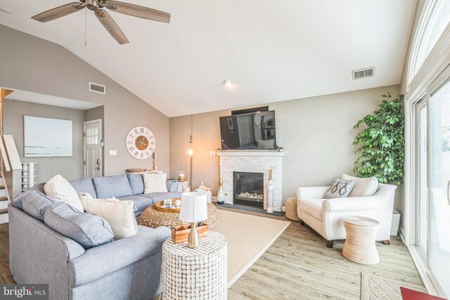 living room featuring ceiling fan, light hardwood / wood-style floors, lofted ceiling, and a fireplace