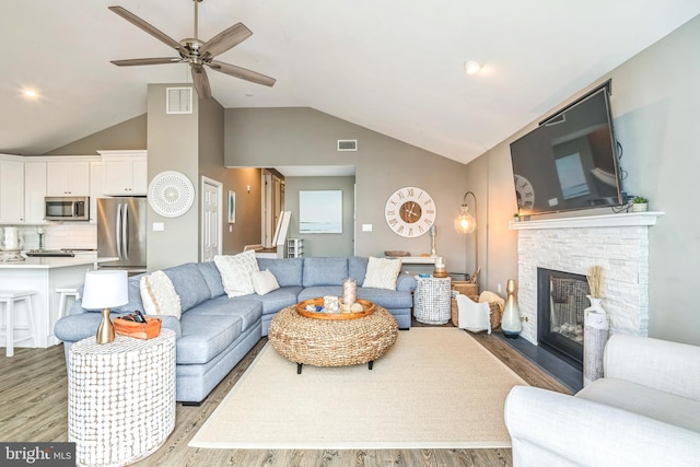 living room with ceiling fan, light hardwood / wood-style floors, a fireplace, and vaulted ceiling