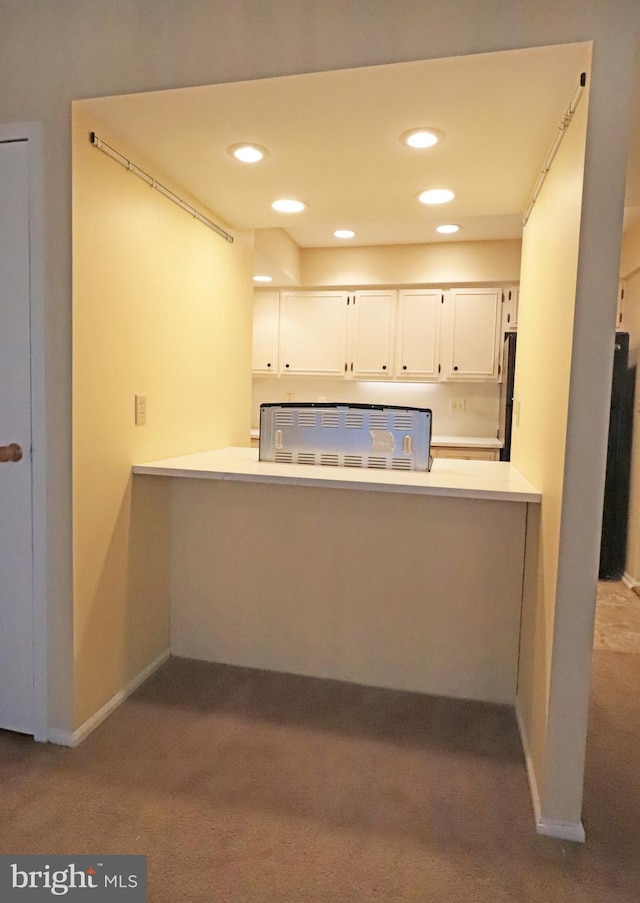 kitchen with kitchen peninsula, light colored carpet, and white cabinetry