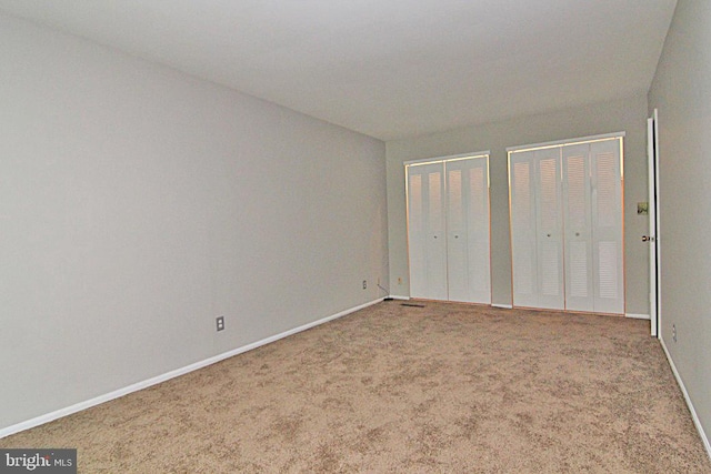 unfurnished bedroom featuring light carpet and multiple closets