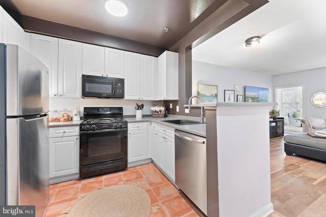 kitchen featuring sink, black appliances, light wood-type flooring, kitchen peninsula, and white cabinets