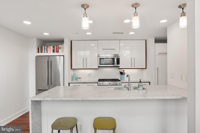 kitchen featuring appliances with stainless steel finishes, a breakfast bar, pendant lighting, white cabinets, and light stone counters