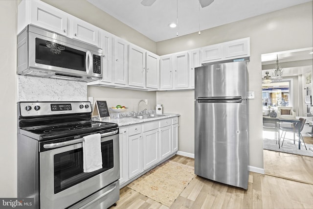 kitchen with ceiling fan with notable chandelier, sink, light hardwood / wood-style flooring, appliances with stainless steel finishes, and white cabinetry