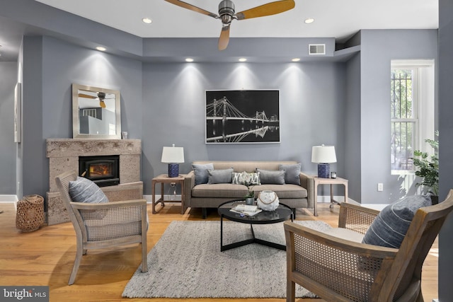 living room with ceiling fan, light wood-type flooring, and a high end fireplace