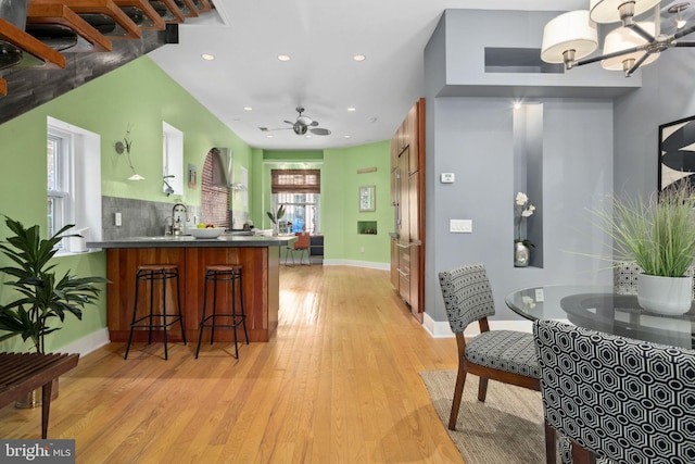 kitchen featuring kitchen peninsula, ceiling fan with notable chandelier, light hardwood / wood-style floors, and a healthy amount of sunlight