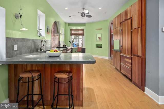 kitchen featuring a kitchen breakfast bar, kitchen peninsula, ceiling fan, and light wood-type flooring