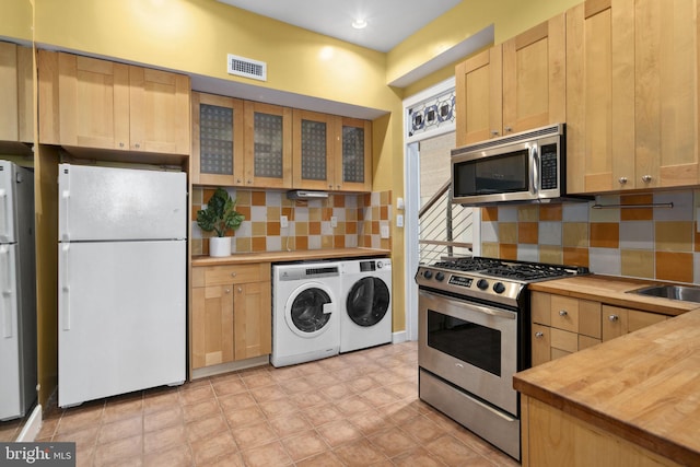 kitchen with appliances with stainless steel finishes, backsplash, light brown cabinetry, washer and dryer, and butcher block countertops