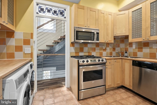 kitchen with light brown cabinets, backsplash, sink, washer / dryer, and stainless steel appliances