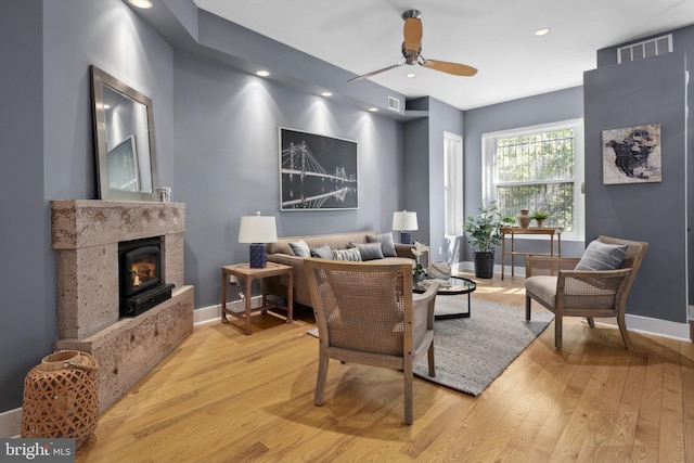 living room with ceiling fan, a premium fireplace, and light hardwood / wood-style flooring