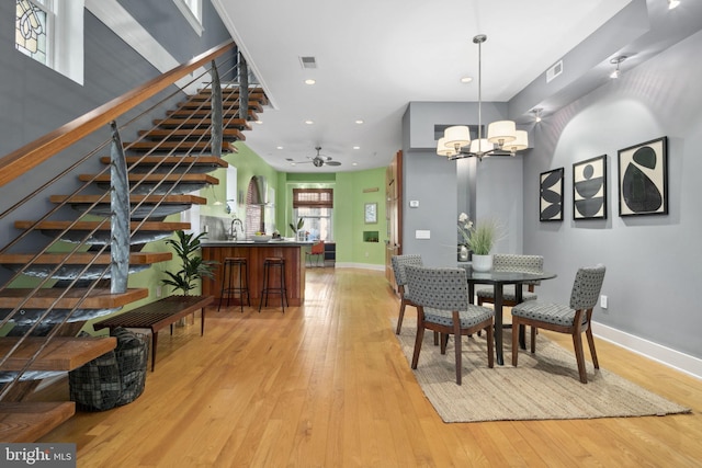 dining space featuring ceiling fan with notable chandelier, light hardwood / wood-style floors, and sink