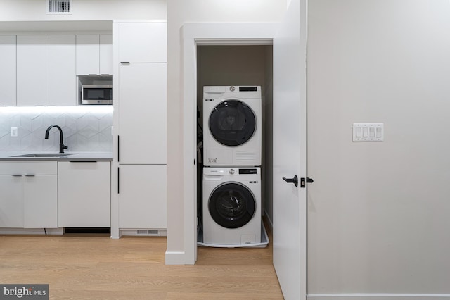 washroom with light hardwood / wood-style flooring, stacked washing maching and dryer, and sink