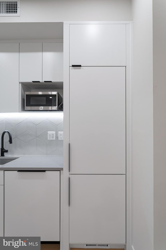 kitchen with decorative backsplash, white cabinetry, and sink