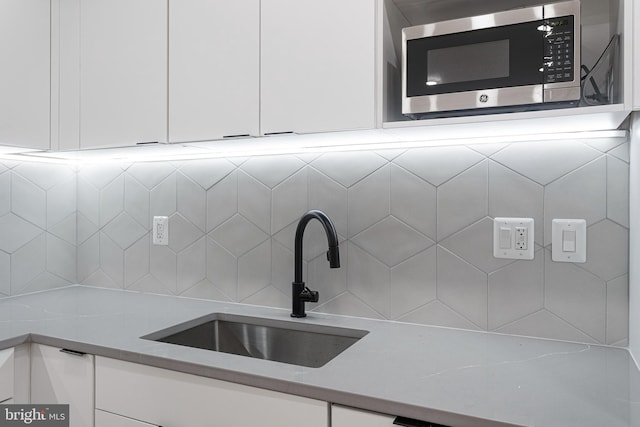 room details with light stone countertops, white cabinetry, stainless steel microwave, and sink