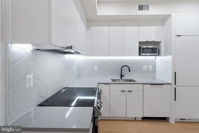 kitchen featuring light wood-type flooring, sink, black range, white cabinetry, and stainless steel microwave