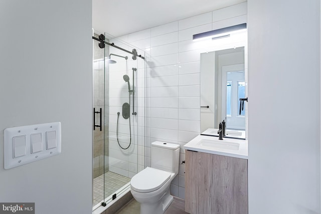 bathroom with vanity, toilet, a shower with shower door, and tile walls