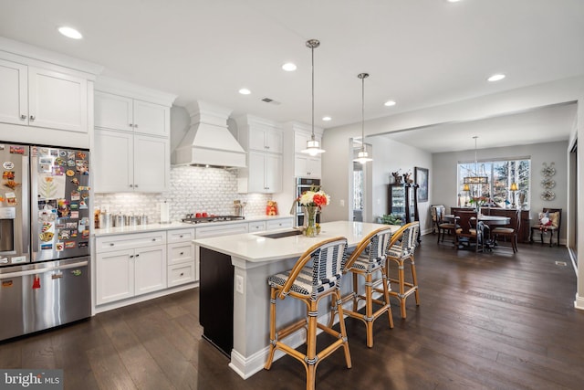 kitchen featuring premium range hood, white cabinets, dark hardwood / wood-style floors, an island with sink, and appliances with stainless steel finishes