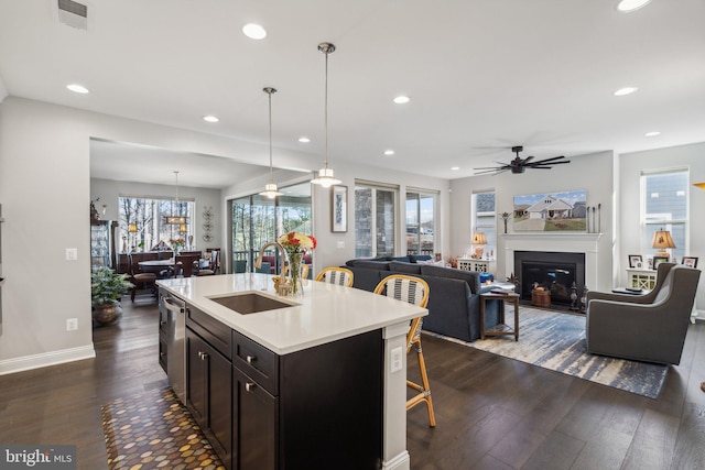 kitchen featuring ceiling fan, sink, dark hardwood / wood-style flooring, pendant lighting, and a kitchen island with sink