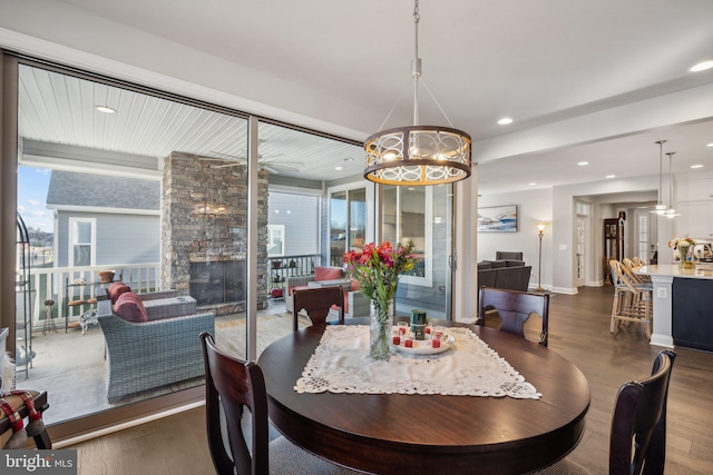 dining space featuring a stone fireplace, dark wood-type flooring, and a notable chandelier