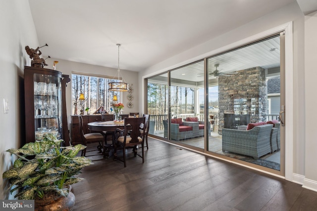 dining room with ceiling fan, a stone fireplace, and dark wood-type flooring