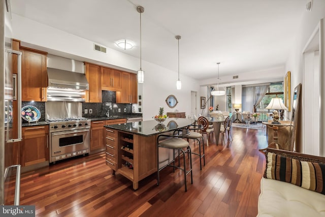 kitchen featuring premium stove, a center island, wall chimney exhaust hood, a kitchen bar, and decorative backsplash