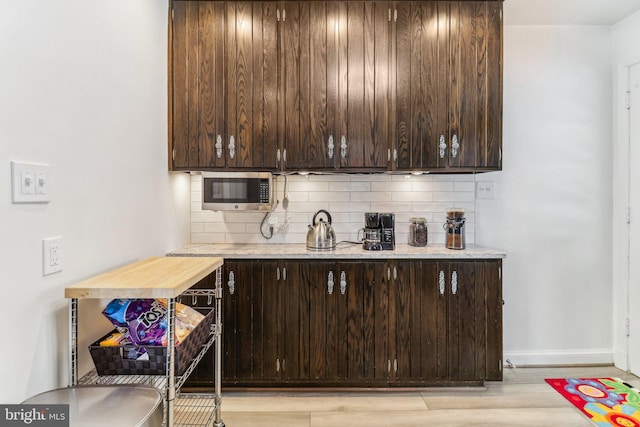 bar with backsplash, light stone counters, dark brown cabinets, and light hardwood / wood-style floors