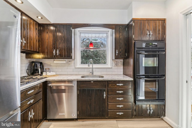 kitchen with dark brown cabinetry, light stone countertops, sink, backsplash, and appliances with stainless steel finishes