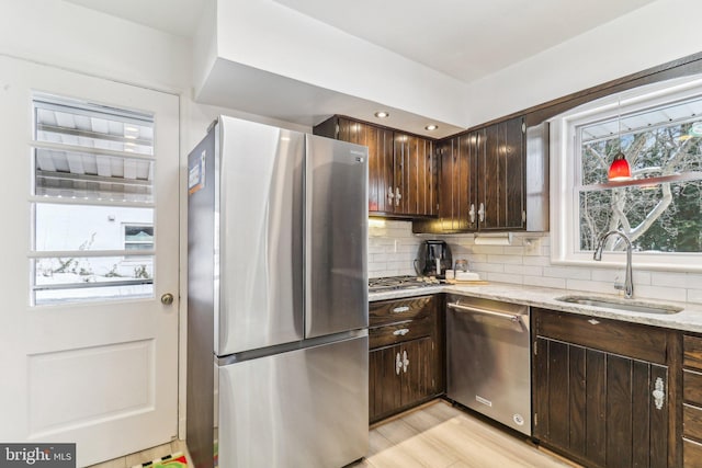 kitchen with sink, decorative backsplash, light stone countertops, dark brown cabinets, and stainless steel appliances