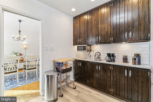 kitchen with light stone countertops, dark brown cabinetry, decorative light fixtures, and light hardwood / wood-style flooring