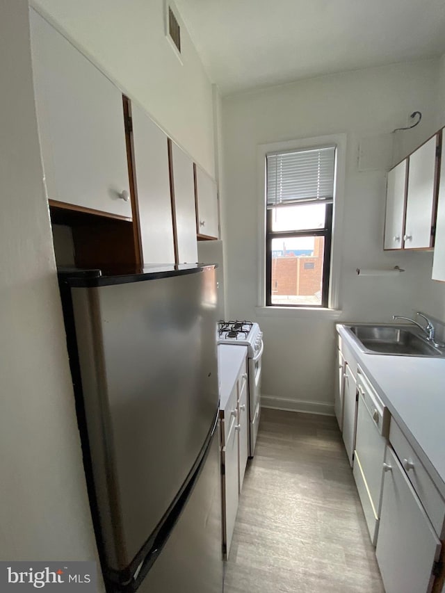 kitchen with white appliances, white cabinetry, sink, and light hardwood / wood-style flooring