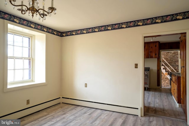 spare room featuring a chandelier, light wood-type flooring, and a baseboard radiator