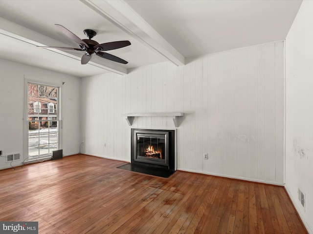 unfurnished living room featuring wooden walls, ceiling fan, wood-type flooring, and beam ceiling