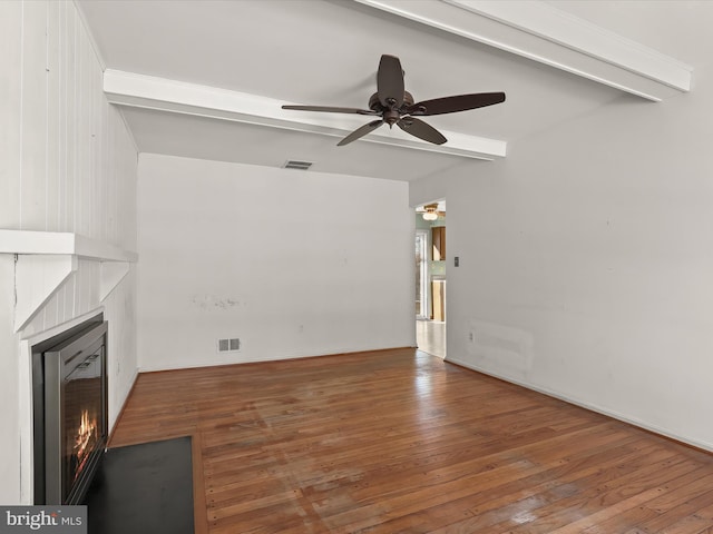 unfurnished living room with a tiled fireplace, ceiling fan, dark wood-type flooring, and beam ceiling