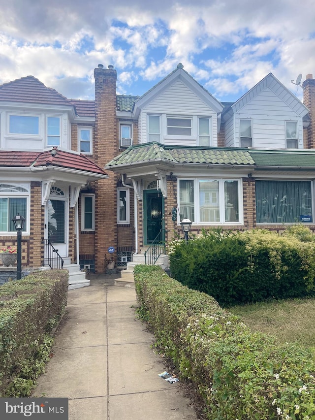 view of front of property featuring entry steps, a tiled roof, a chimney, and brick siding