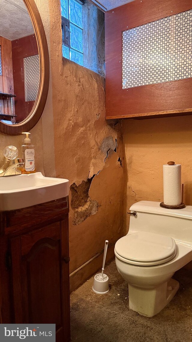 half bathroom with a textured wall, vanity, toilet, and a textured ceiling